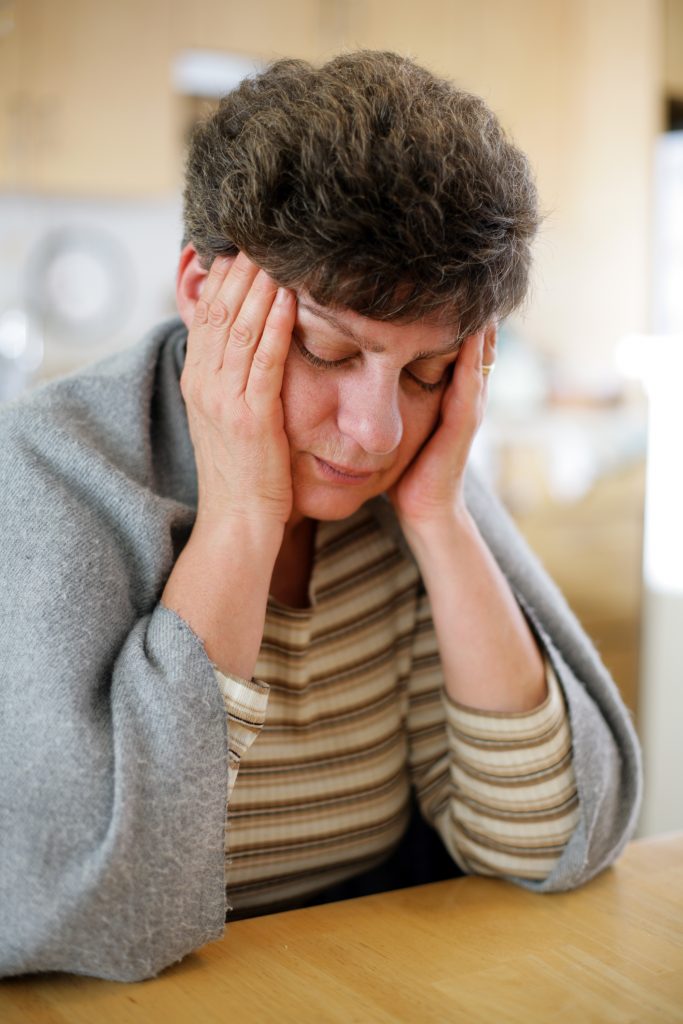 Woman sitting at a table with a blanket around her shoulders and her hands on her face Woman sitting at a table with a blanket around her shoulders and her hands on her face